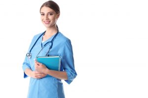 RN nurse wearing blue scrubs while holding blue noteboks which she uses to study to get her BSN degree. Nurse wearing stethoscope on neck.