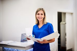 med tech woman wearing blue and holding binder while smiling