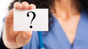 selective focus of a nurse holding a question sign card at the camera signifying the questions related towards a nursing degree
