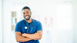 A smiling CNA with his arms crossed. Image demonstrates the important of a positive attitude for CNAs.