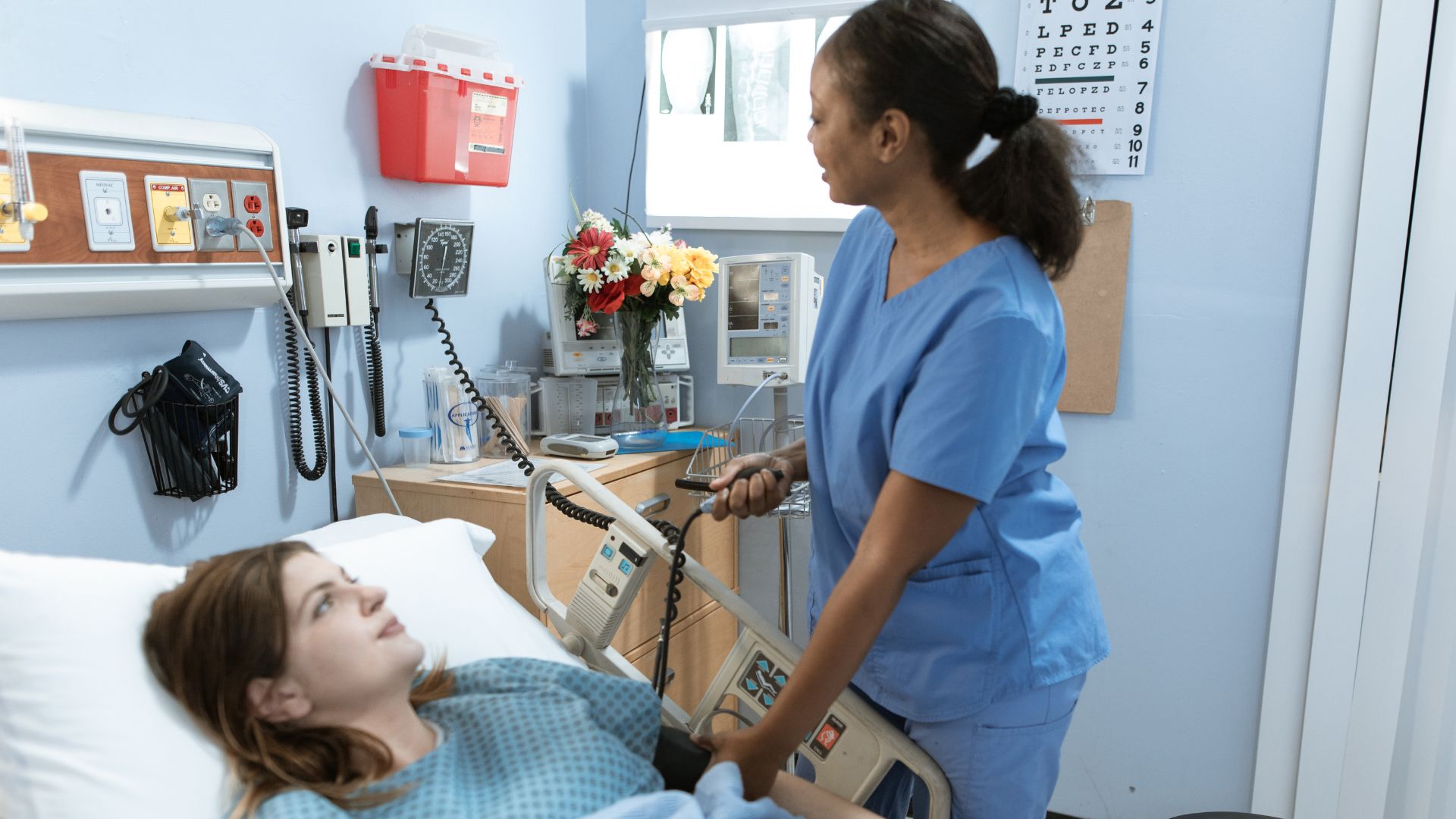 A registered nurse dutifully tends to her patient, who's laid back in her bed. Image demonstrates the importance of bedside manner for registered nurses.