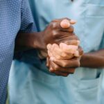 two sets of hands holding one another, one nurse and one older patient