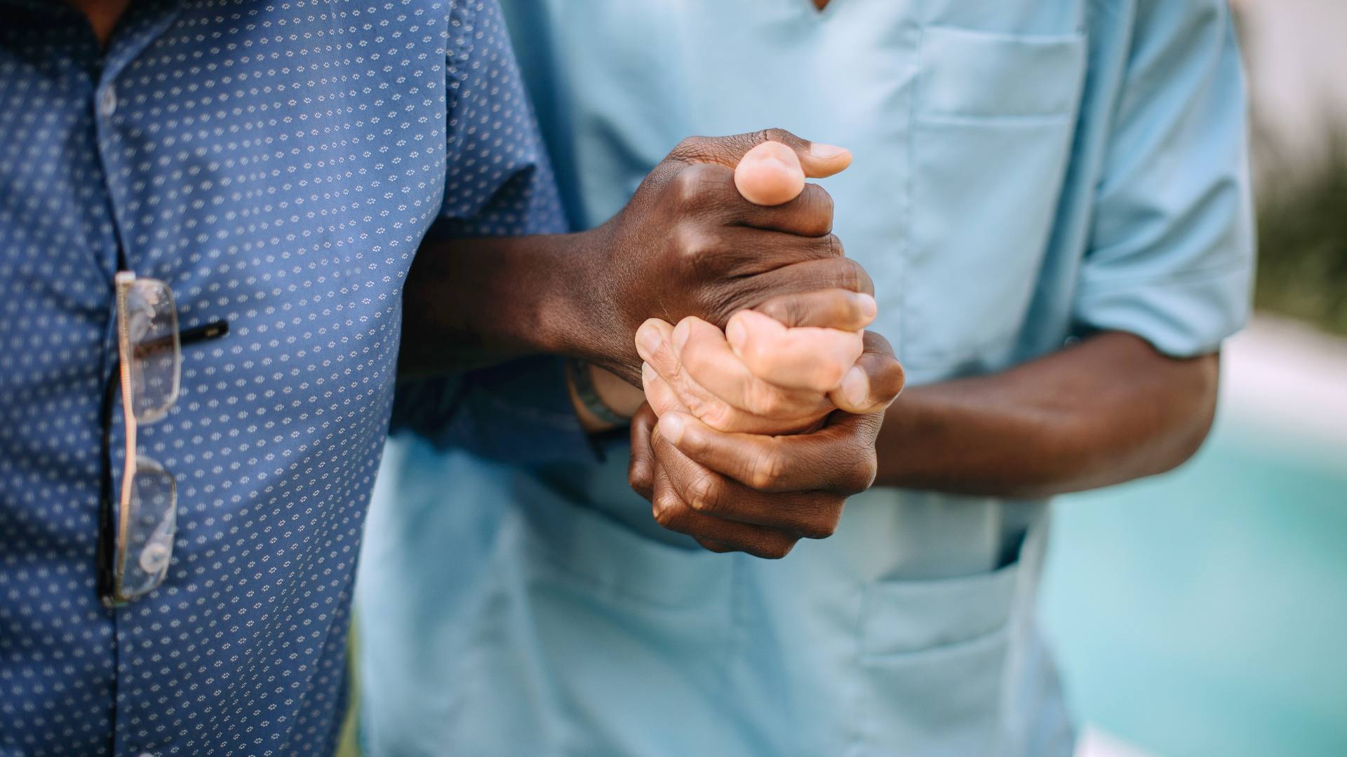 two sets of hands holding one another, one nurse and one older patient