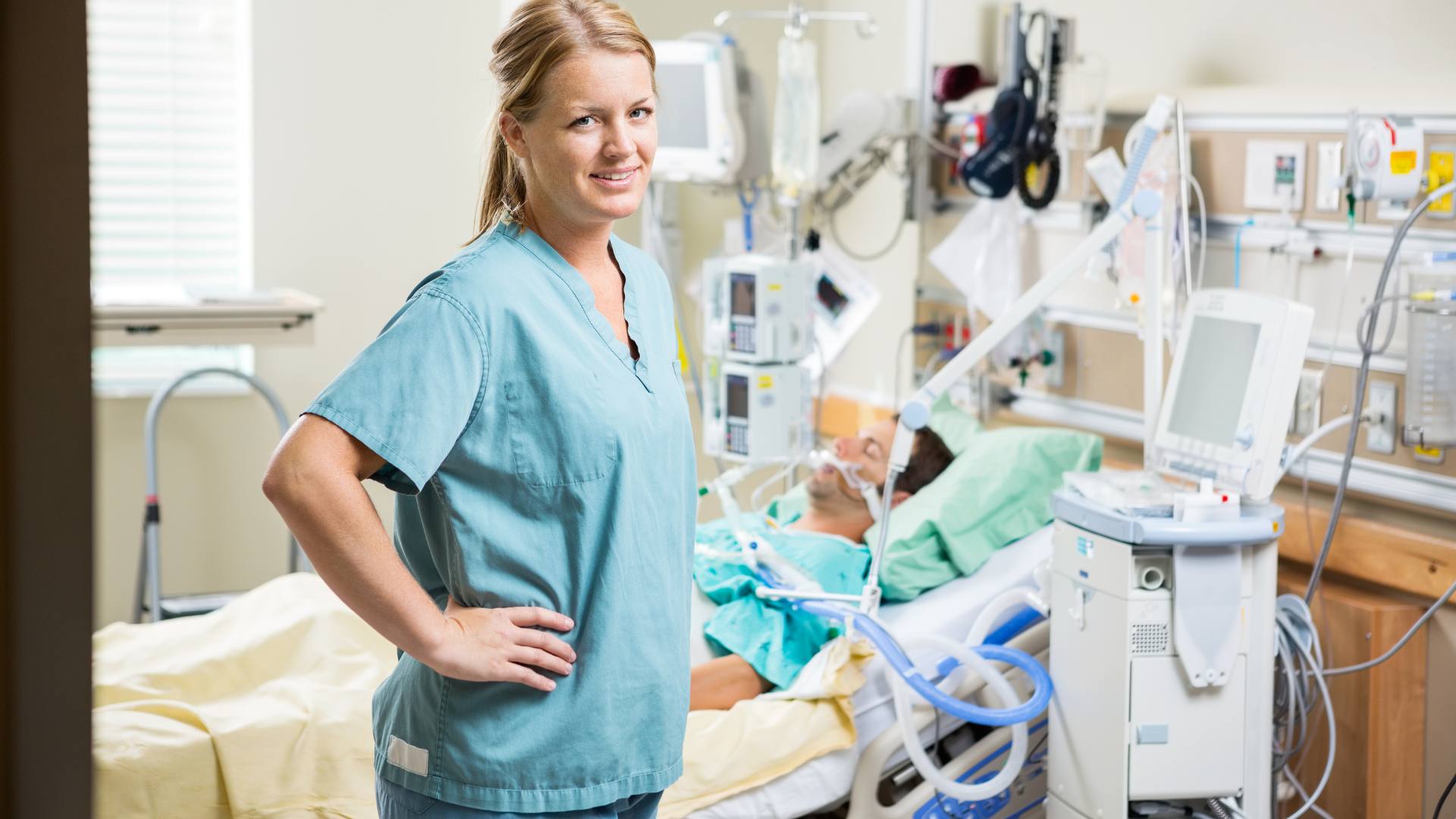 A nurse in an ICU room stands in front of a patient, demonstrating the job of a critical care nurse.