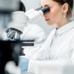 A med tech sits in a lab and looks through a microscope.
