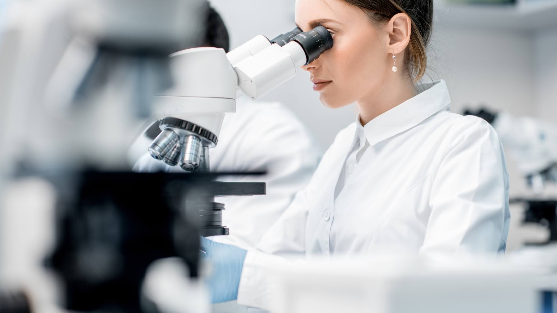 A med tech sits in a lab and looks through a microscope.