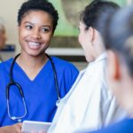 A nurse wearing blue scrubs smiles at a coworker.