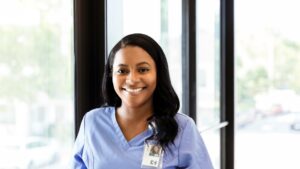 An RN is pictured smiling in scrubs, demonstrating being an RN in assisted living facilities.