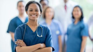 A nurse wears blue scrubs and a stethoscope around her neck while smiling with her arms crossed, demonstrating successful nursing placement.