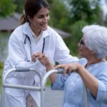 A med tech at a nursing home assists a patient outside with her walker.