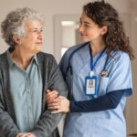 A licensed practical nurse smiles while holding the arm of a senior resident, demonstrating the role of licensed practical nurses in senior living communities.