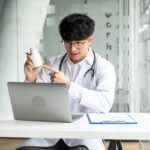 A person wearing a white lab coat sits at a desk and holds up a medication bottle, demonstrating med tech classes.